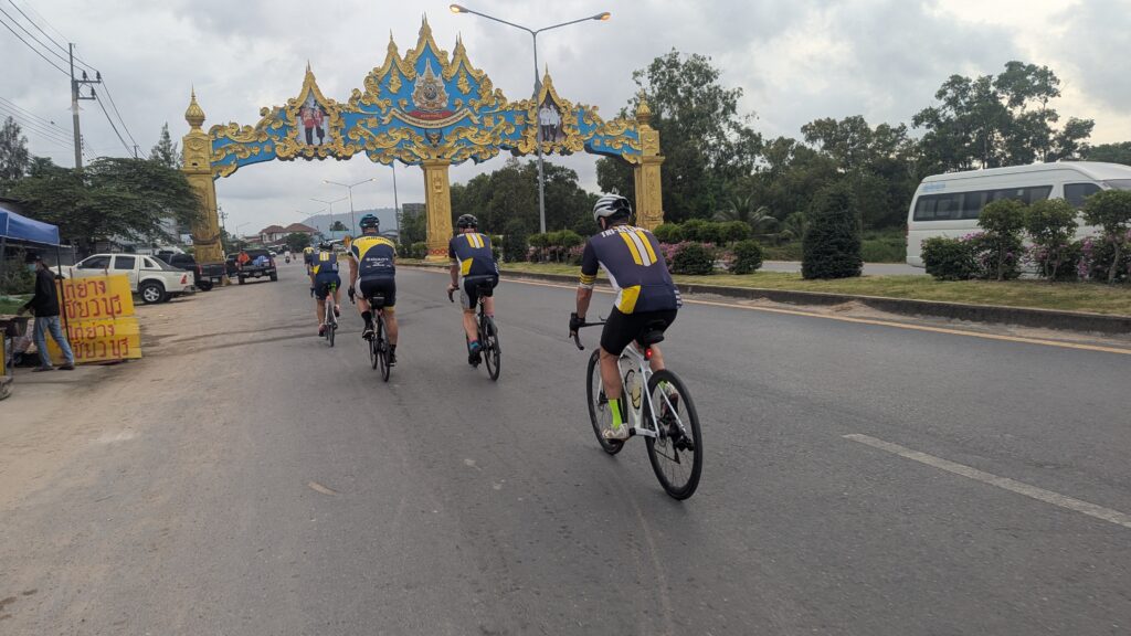 Tri Alliance riders cycling beneath an ornate gateway in Thailand